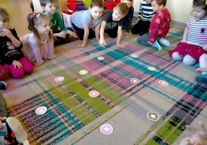 Dzieci oglądają sylwety pączków porozkładane na dywanie.