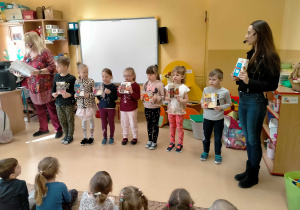 Dzieci stoją, trzymając w rękach pudełka po różnych kaszach i śpiewają piosenkę o kaszach z p.Ulą i p.Agą..