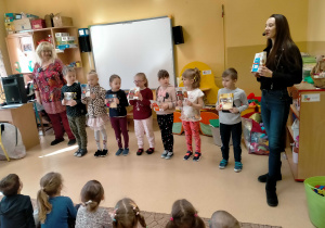 Dzieci stoją, trzymając w rękach pudełka po różnych kaszach i śpiewają piosenkę o kaszach z p.Ulą i p.Agą..