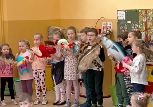 Dzieci stoją trzymając w rękach pluszowe ryby i śpiewając o nich piosenkę.