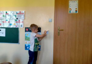 Chłopiec odczepia kopertę nr.1 ze ściany.