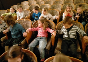 Dzieci siedzą na fotelach teatralnych.
