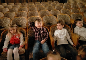 Dzieci siedzą na fotelach teatralnych.