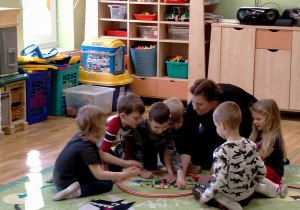 Dzieci siedzą z p.Olą na dywanie i oglądają pomponiki w obręczy.