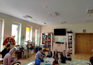 Dzieci siedzą z p. Martą na dywanie i omawiają obrazki o tematyce wiosenej.