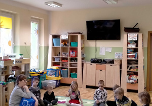 Dzieci siedzą z p. Martą na dywanie i tworzą historyjki na podstawie ilustracji.