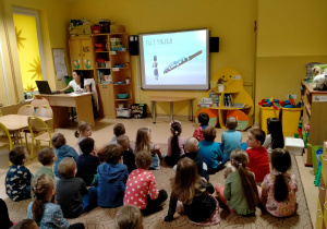 Dzieci słuchają melodii granej na flecie picolo oraz ogladają go na zdjęciu.