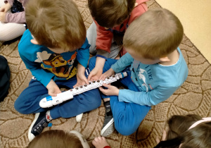 Dzieci oglądają dziecięcy flet poprzeczny oraz przyciskają znajdujące się na nim klapki.