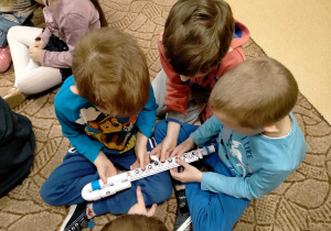 Dzieci oglądają dziecięcy flet poprzeczny oraz przyciskają znajdujące się na nim klapki.