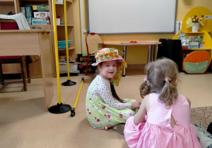 Dziewczynka w wiosennym kapeluszu siedzi na dywanie.