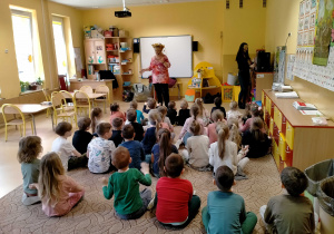 Dzieci siedzą na dywanie i słuchają piosenki śpiewanej przez p.Ulę.