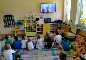 Dzieci siedzą na dywanie i słuchają piosenki śpiewanej przez p.Witka