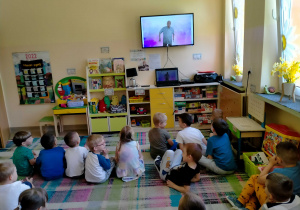 Dzieci siedzą na dywanie i słuchają piosenki śpiewanej przez p.Witka.