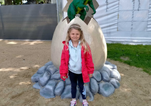 Dziewczynka stoi przy jajku z którego wykluwa się dinozaur.