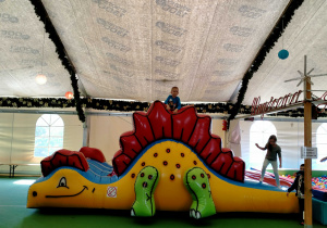 Chłopiec zjeżdża na dmuchanej zjeżdżalni w kształcie dinozaura.