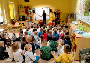 Dzieci siedzą na dywanie i słuchają piosenki śpiewanej przez p.Ulę i Agnieszkę.