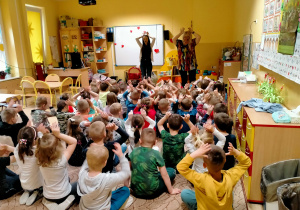 Dzieci siedzą na dywanie i naśladują ruchy pokazywane przez p.Ulę i Agnieszkę.