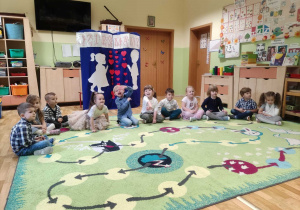 Dzieci siedza na dywanie przy dekoracji z okazji "Dnia Mamy i Taty".