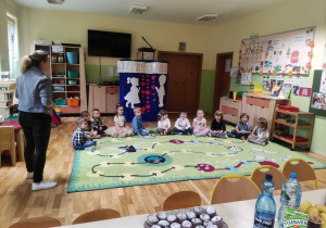 Dzieci siedzą na dywanie przy dekoracji z okazji "Dnia Mamy i Taty".