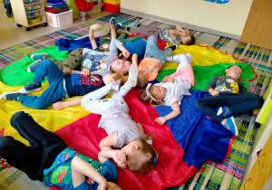 Dzieci odpoczywają, leżąc na chuście animacyjnej.