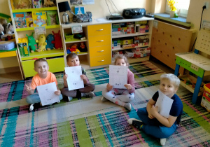 Dzieci siedzą na dywanie i pokazują certyfikaty "SUPER DZIECKA"