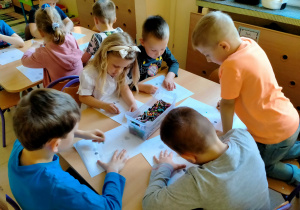 Dzieci kolorują i ozdabiają certyfikaty "SUPER DZIECKA" przy stoliku.