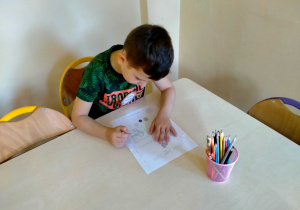 Chłopiec koloruje i ozdabia certyfikat "SUPER DZIECKA" przy stoliku.