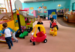 Dzieci jeżdżą pojazdami po sali.
