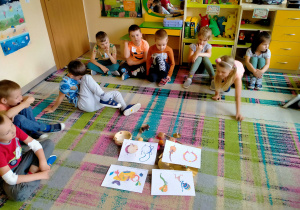 Dzieci siedzą w kole i oglądają ilustracje instrumentów do piosenki "Magiczny kuferek".