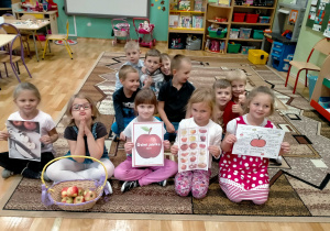 Dzieci pozują do pamiątkowego zdjęcia trzymając w rękach informacje na temat jabłek i kosz z jabłkami.