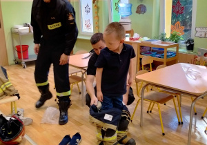 Chłopiec przymierza strój strażacki wykorzystywany podczas akcji pożarniczej.