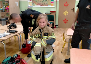 Dziewczynka w stroju strażackim wykorzystywanym podczas akcji pożarniczej.
