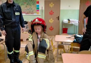 Dziewczynka w stroju strażackim wykorzystywanym podczas akcji pożarniczej.
