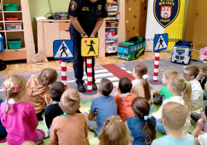 Strażnik miejski pokazuje dzieciom znaki "Uwaga piesi" i "Agatka"