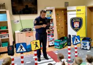 Strażnik miejski omawia dzieciom sygnalizator dla pieszych.
