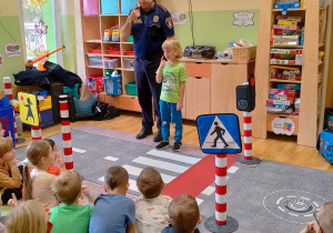 Strażnik miejski i chłopiec, pokazują dzieciom jak zapamiętać numer 112 pokazując go na swojej buzi.