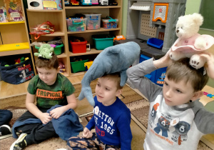 Dzieci sadzają misia na swojej głowie.