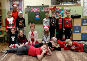 "Mikołajkowe" zdjęcie grupowe przy dekoracji tematycznej. Dzieci są w świąteczno-mikołajowych ubraniach.