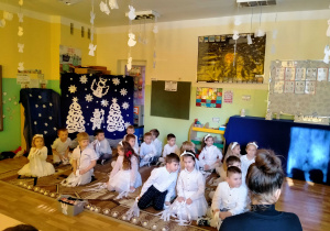 Dzieci siedzą na dywanie przy świątecznej dekoracji.