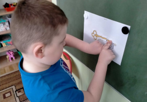 Chłopiec przykleja 4 część klucza na jego sylwetę.