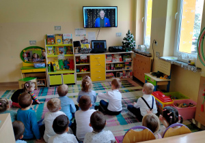 Dzieci siedzą na dywanie i słuchają p. Witka.