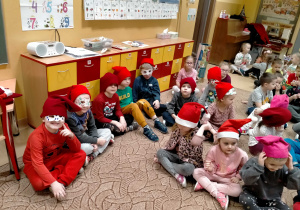 Dzieci siedzą na dywanie maja na twarzach karnawałowe maski a na głowach czapki krasnali.