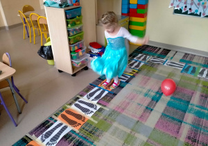 Dziewczynka porusza się przy muzyce po "śladach" na dywanie.