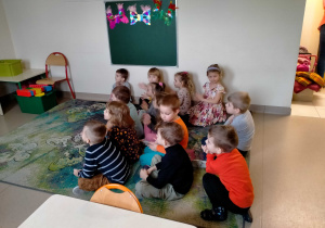 Dzieci siedzą na dywanie i słuchają koncertu.