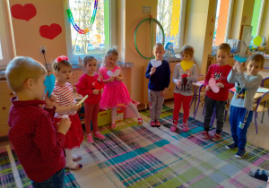 Dzieci stoją w kole i trzymają w rękach serca w różnych kolorach.