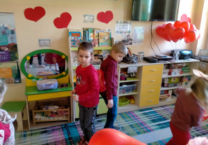 Chłopcy tańczą w parze, trzymając serduszkowy balon między plecami.
