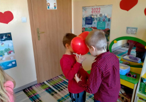 Chłopcy tańczą w parze, trzymając serduszkowy balon między głowami.