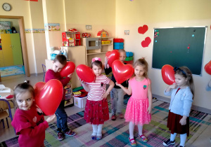 Dzieci stoją i dotykają serduszkowymi balonami do ucha.