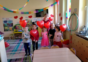 Dzieci stoją z panią Martą, trzymając serduszkowe balony w rękach.