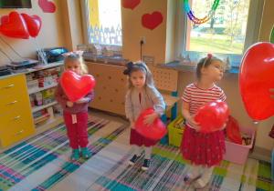 Dziewczynki tańczą z serduszkowym balonem w rękach.